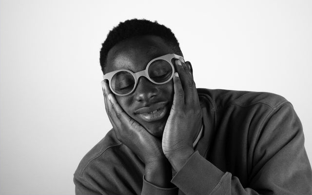 A model wearing REFRAMD round-frame glasses with hands gently placed on cheeks, captured in a serene, black-and-white portrait.