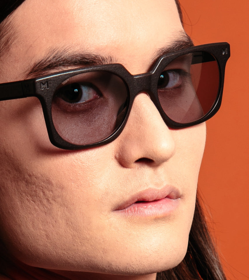Close-up of a person wearing black sunglasses with an orange background