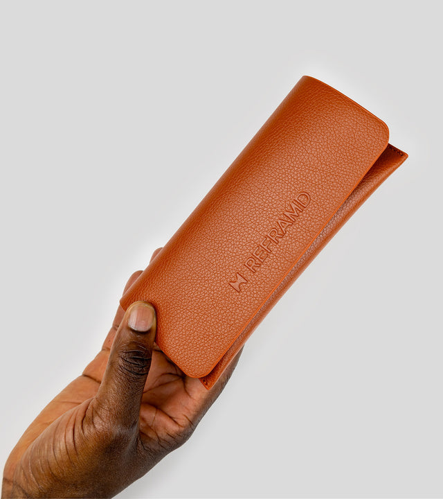 Brown leather sunglasses pouch held by a hand on a light gray background