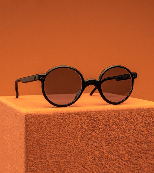 REFRAMD Black round sunglasses on an orange surface with an orange background