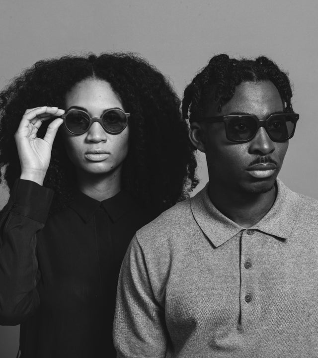 Monochrome fashion portrait of a stylish woman with curly hair and a man with dreadlocks both wearing designer sunglasses, showcasing urban chic eyewear in a black and white photograph