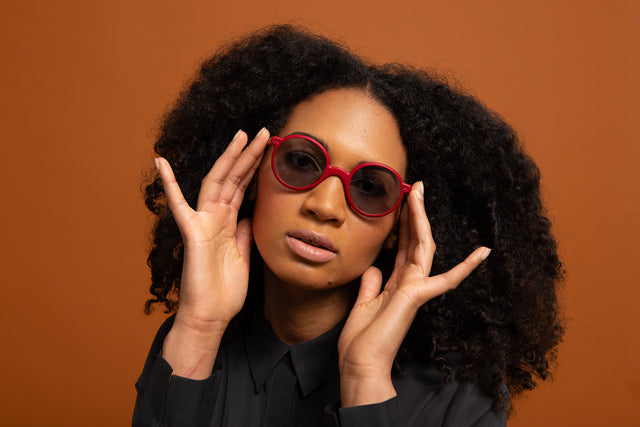 Model with curly hair wearing red REFRAMD 3D-printed sunglasses against an orange background, showcasing modern eyewear design