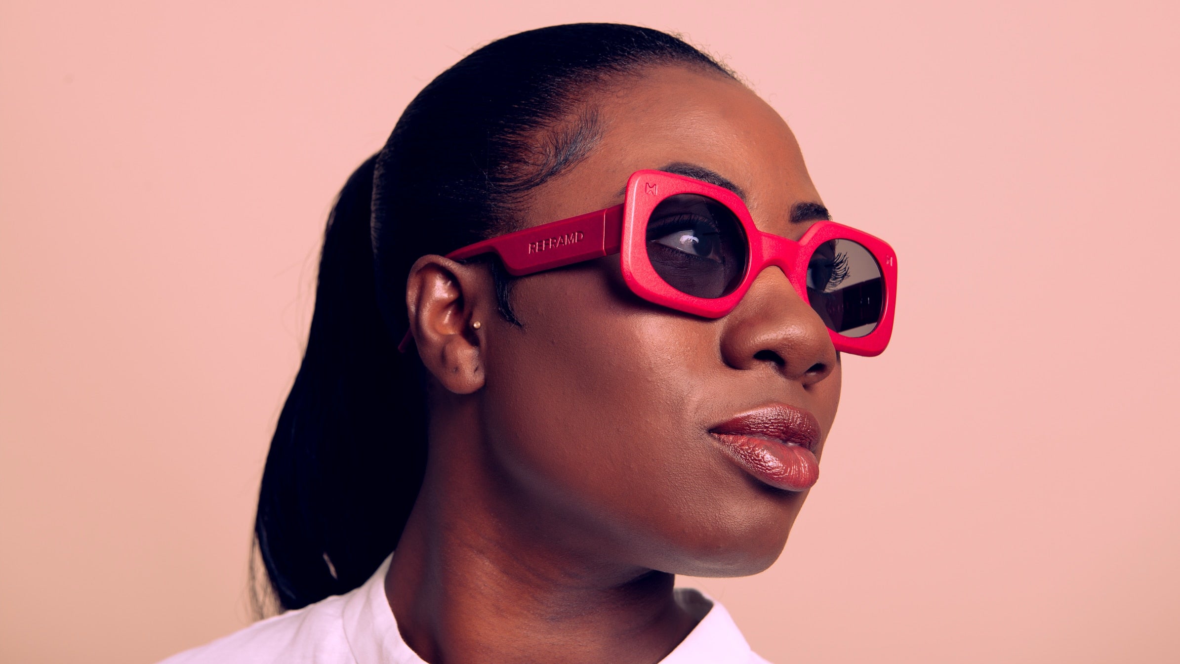 Woman wearing pink sunglasses against a beige background