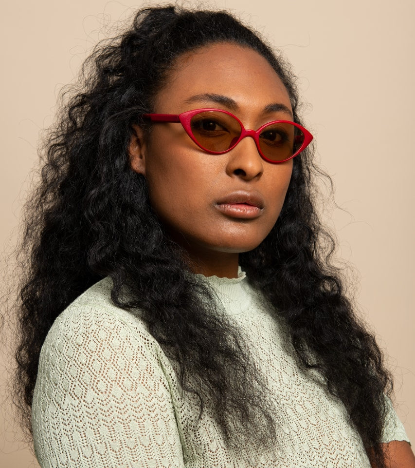Woman wearing red sunglasses with a beige background