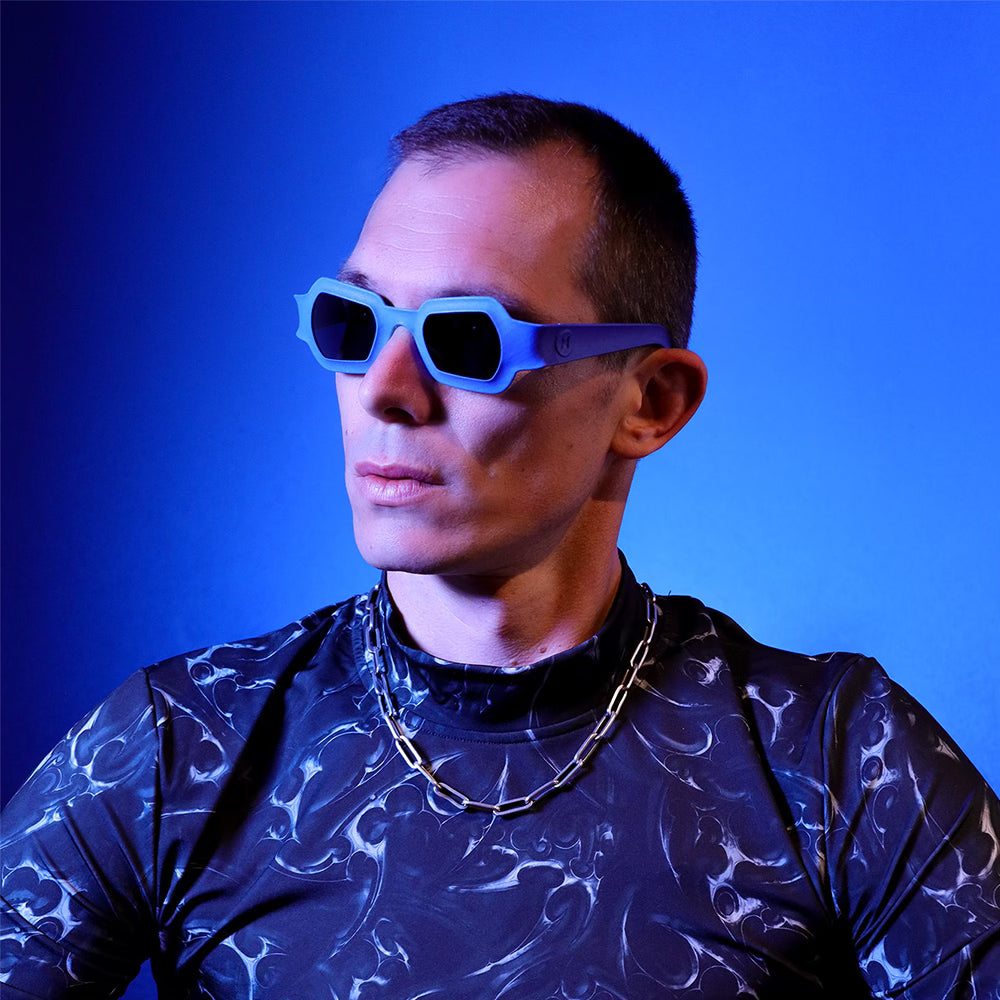 Male model in blue lighting wearing space-print shirt and bold blue REFRAMD sunglasses, futuristic fashion style